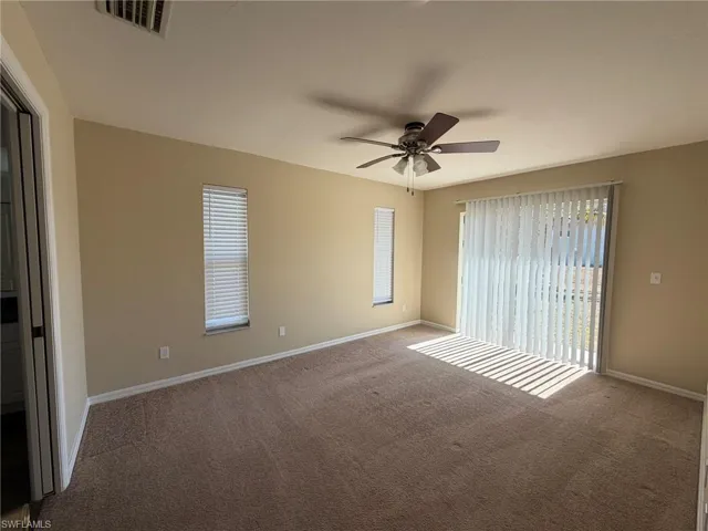 Carpeted spare room featuring ceiling fan and baseboards
