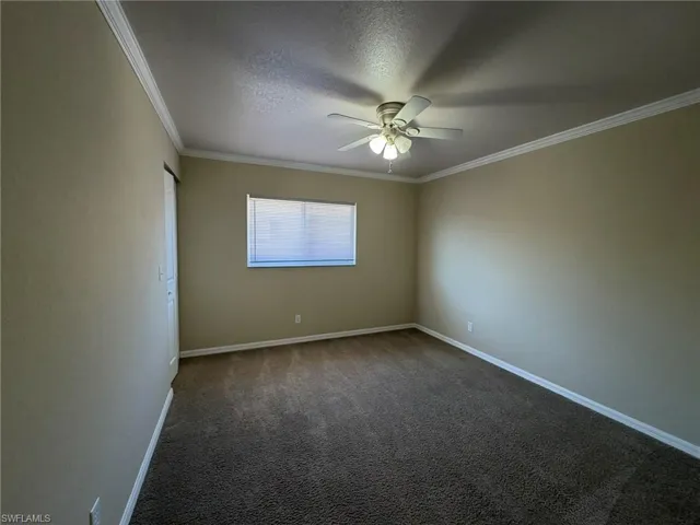 Empty room featuring a ceiling fan, dark carpet, ornamental molding, and a textured ceiling