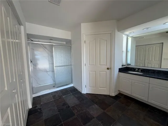 Full bath with vanity, a marble finish shower, and dark stone finish floors