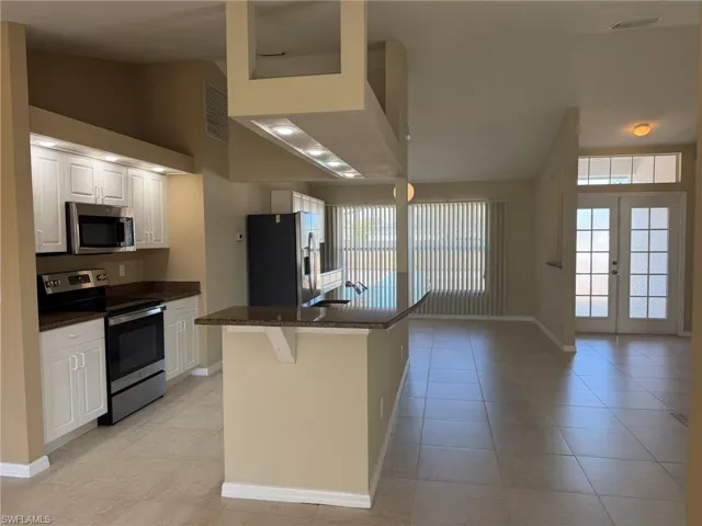 Kitchen featuring stainless steel appliances, white cabinetry, french doors, a center island with sink, and vaulted ceiling