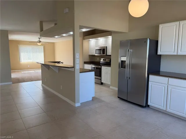 Kitchen featuring stainless steel appliances, white cabinetry, a high ceiling, a kitchen breakfast bar, and ceiling fan