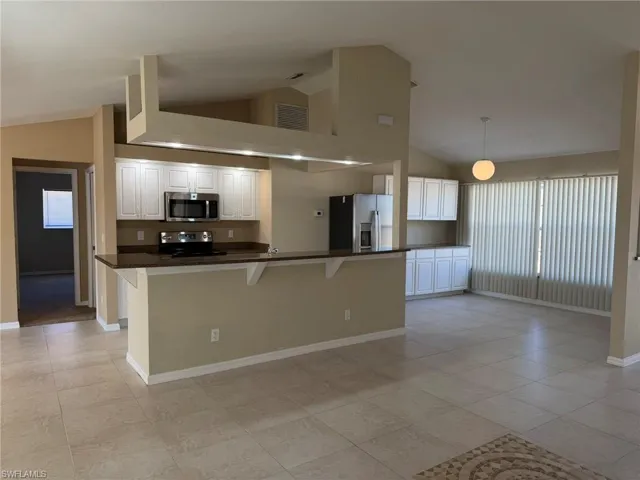 Kitchen with a breakfast bar, vaulted ceiling, stainless steel appliances, white cabinets, and decorative light fixtures