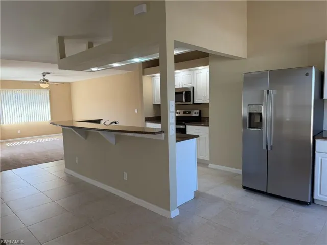 Kitchen featuring stainless steel appliances, white cabinets, a kitchen breakfast bar, a ceiling fan, and a high ceiling