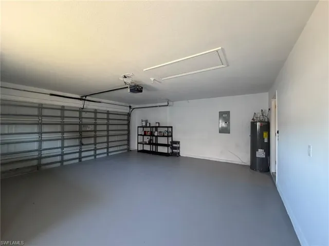 Garage featuring electric water heater, electric panel, and a garage door opener