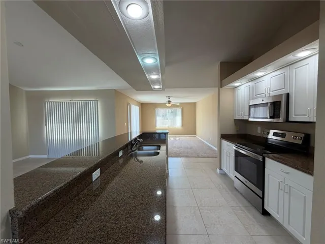 Kitchen featuring stainless steel appliances, dark stone counters, white cabinets, light tile patterned flooring, and recessed lighting