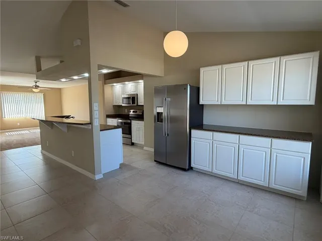 Kitchen with vaulted ceiling, white cabinets, stainless steel appliances, decorative light fixtures, and a breakfast bar area