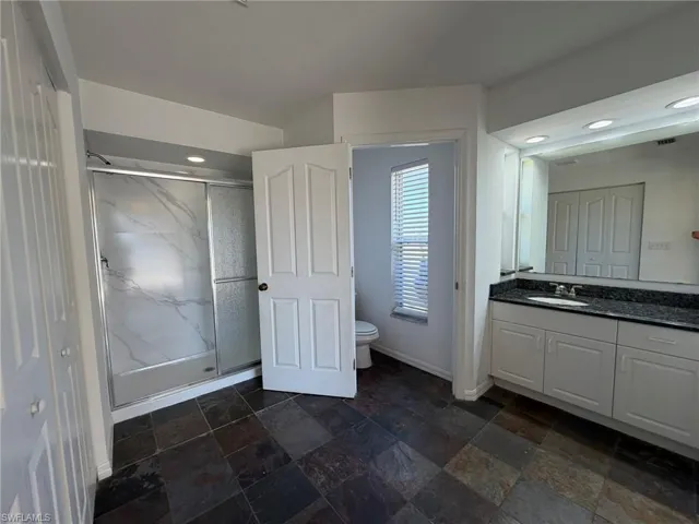 Bathroom featuring vanity, a marble finish shower, stone tile floors, and recessed lighting