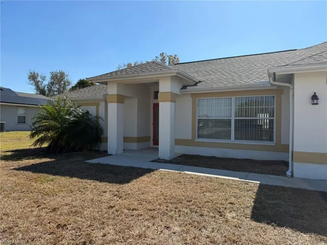 Property entrance with a shingled roof, a yard, and stucco siding