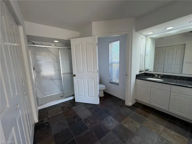 Bathroom featuring vanity, a marble finish shower, stone tile floors, and recessed lighting