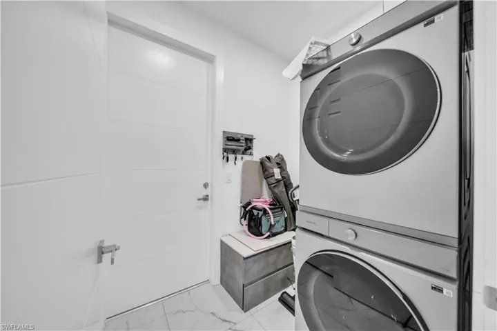Laundry room with stacked washer and dryer and light marble finish flooring