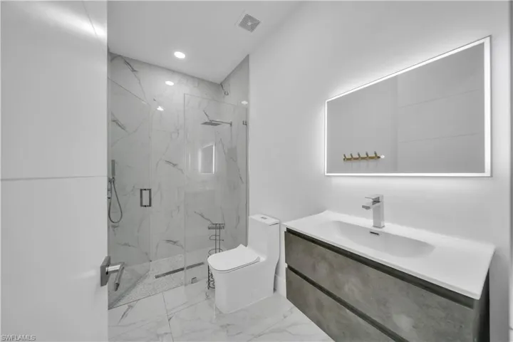 Full bathroom featuring vanity, a marble finish shower, recessed lighting, and light marble finish flooring