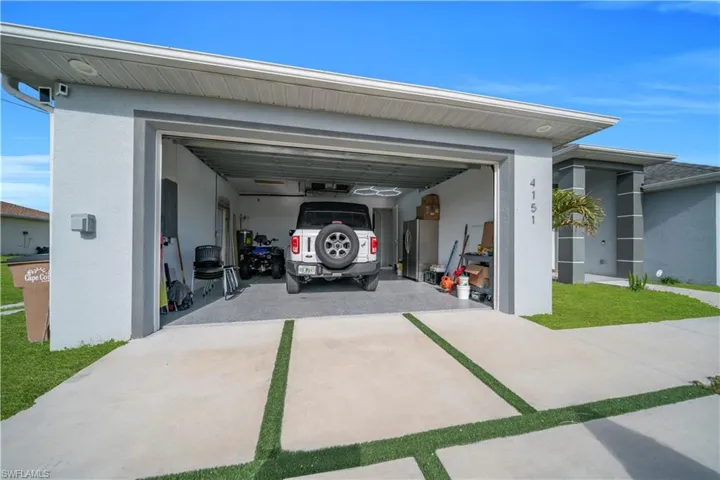 Garage featuring freestanding refrigerator, concrete driveway, and electric panel