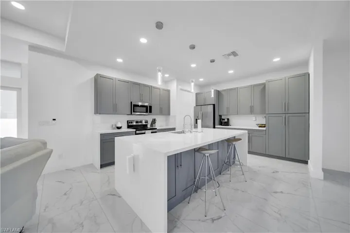 Kitchen featuring gray cabinets, a breakfast bar area, an island with sink, light stone counters, and stainless steel appliances