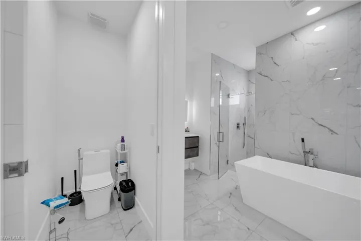 Full bathroom with vanity, a marble finish shower, a freestanding tub, recessed lighting, and light marble finish floors