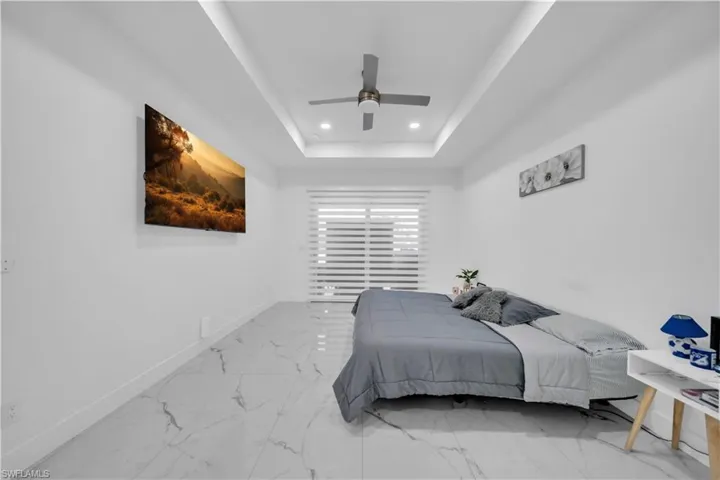 Bedroom featuring ceiling fan, recessed lighting, light marble finish flooring, and a tray ceiling