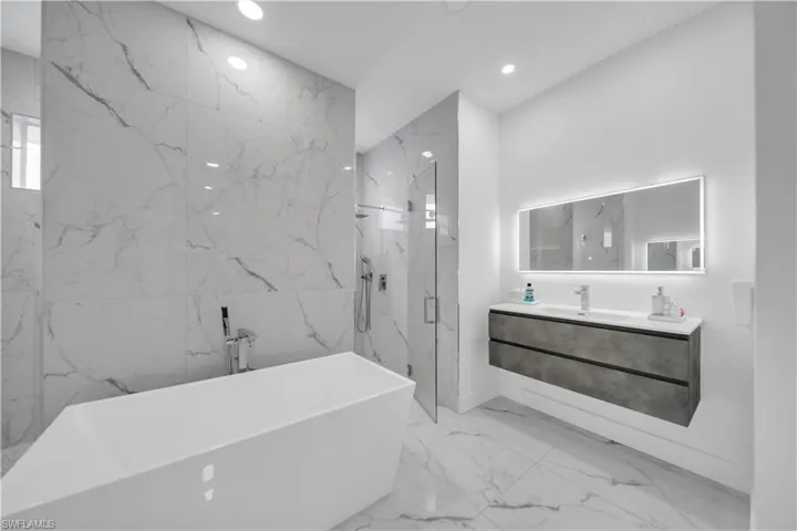 Bathroom with a marble finish shower, a freestanding tub, vanity, stone wall, and recessed lighting