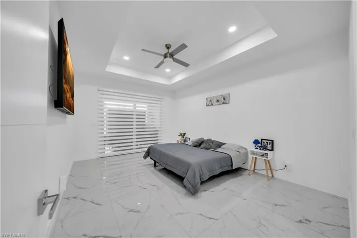 Bedroom with recessed lighting, light marble finish flooring, ceiling fan, and a raised ceiling