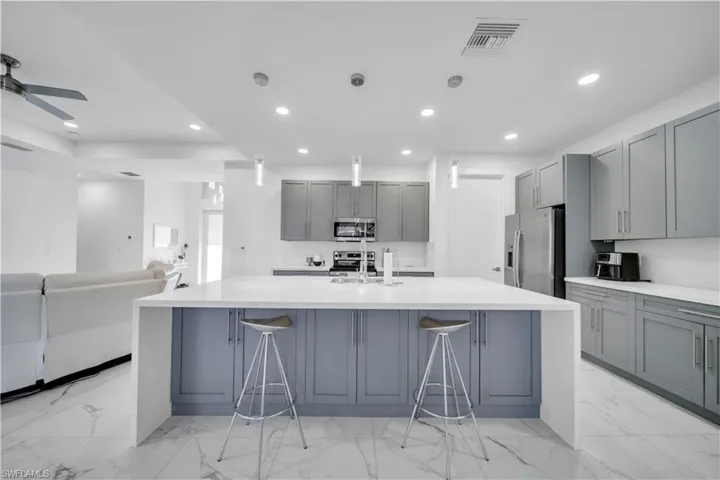 Kitchen with gray cabinets, light stone countertops, a large island, and stainless steel appliances