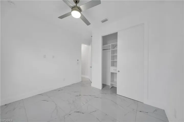 Unfurnished bedroom featuring light marble finish floors, a ceiling fan, and a closet