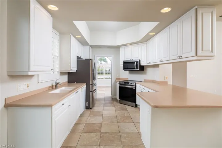Kitchen with recessed lighting, a peninsula, a sink, white cabinets, and appliances with stainless steel finishes