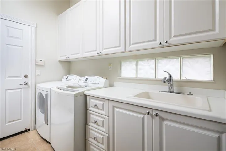 Laundry area with cabinet space, light tile patterned floors, a sink, and washing machine and clothes dryer