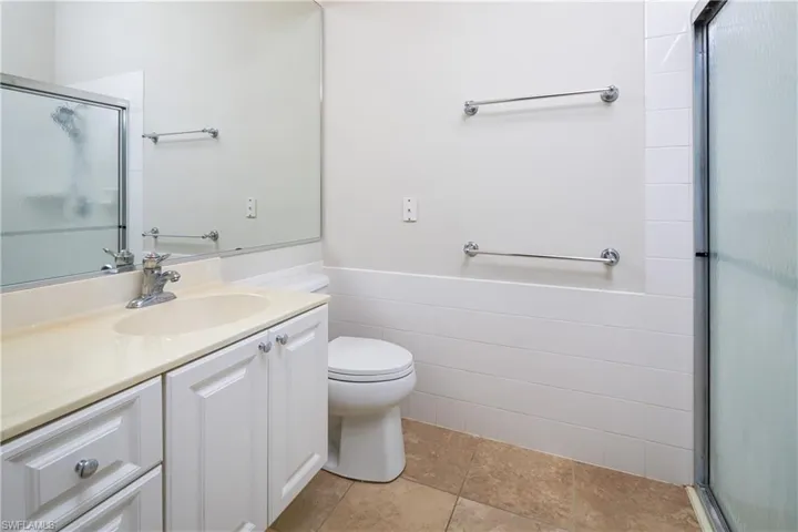 Primary bathroom with a shower with shower door, toilet, vanity, tile walls, and wainscoting