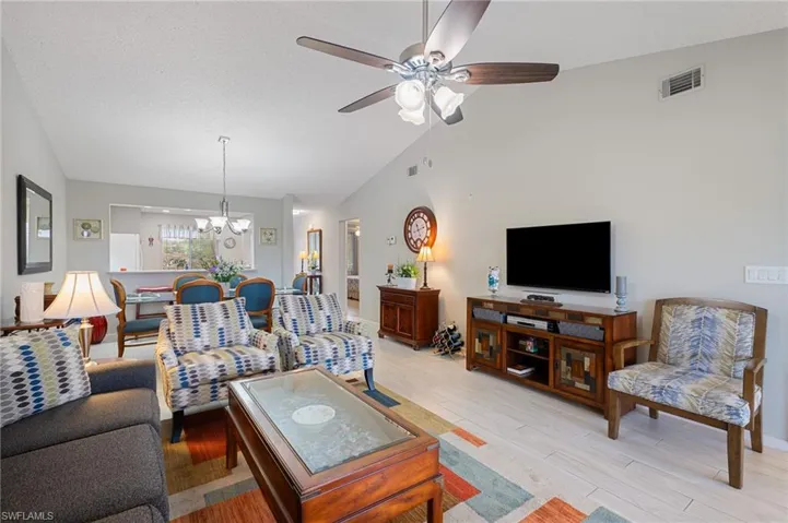Living room with ceiling fan with notable chandelier, light wood-type flooring, and vaulted ceiling