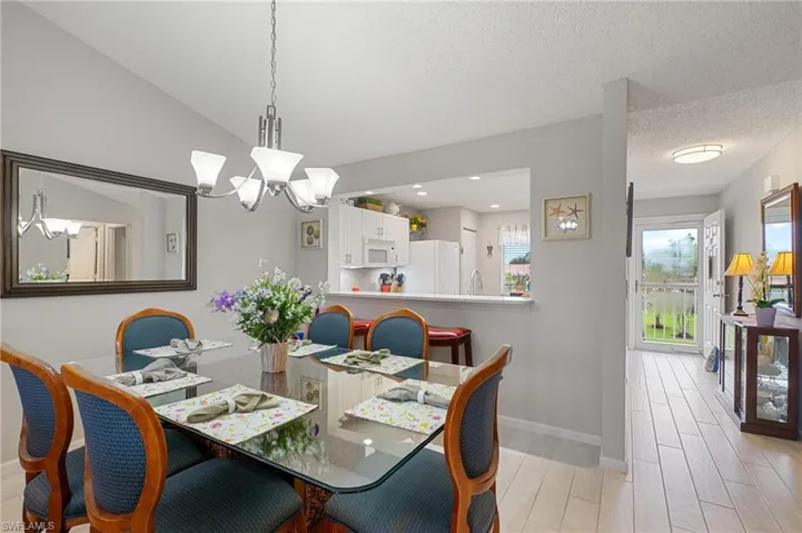Dining space featuring light hardwood / wood-style flooring, vaulted ceiling, sink, a textured ceiling, and an inviting chandelier