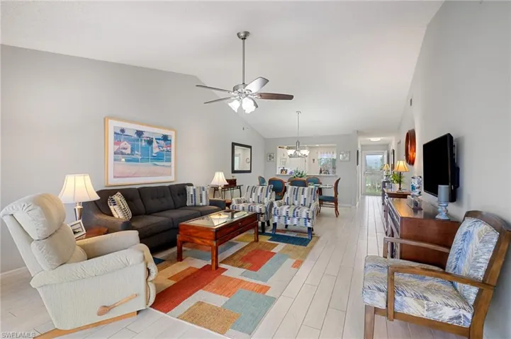 Living room featuring light hardwood / wood-style floors, ceiling fan with notable chandelier, and vaulted ceiling