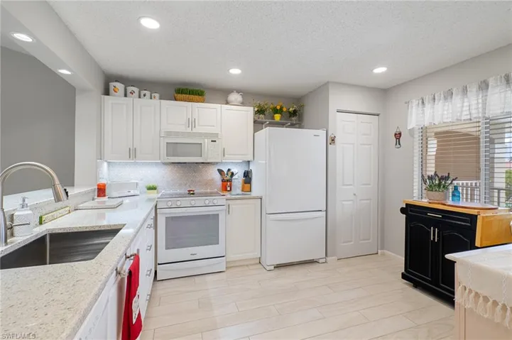 Kitchen featuring white appliances, light stone countertops, a textured ceiling, white cabinetry, and sink