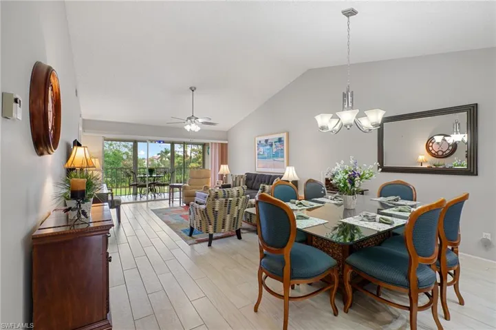 Dining room with vaulted ceiling, ceiling fan with notable chandelier, and light hardwood / wood-style flooring