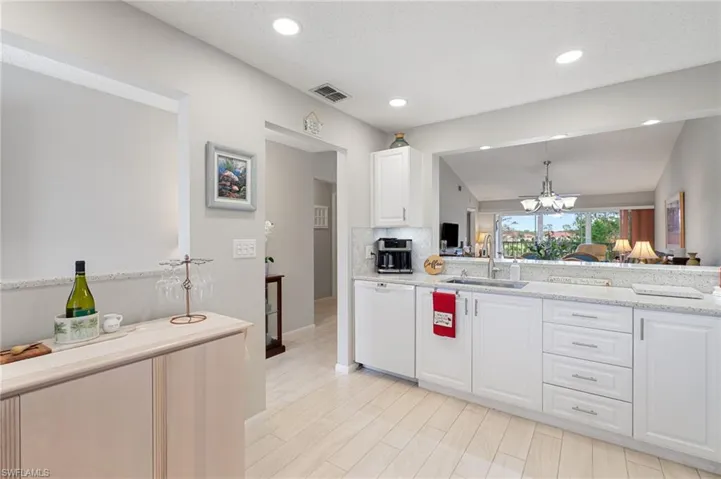 Kitchen featuring white dishwasher, a chandelier, sink, white cabinets, and pendant lighting