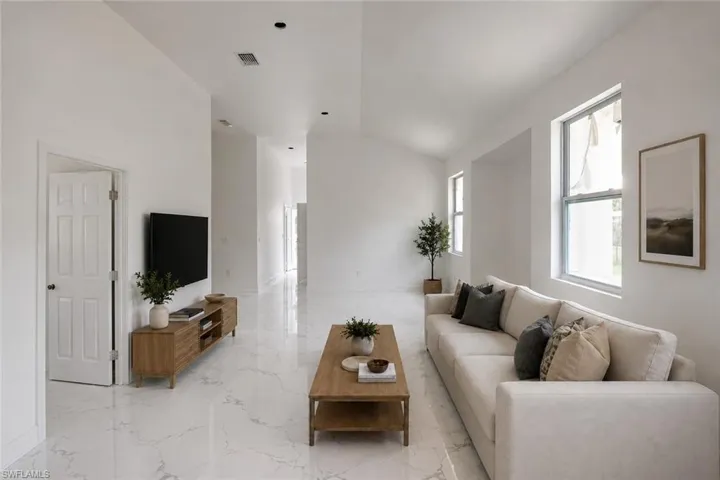 Open concept living area featuring white marble-look flooring, recessed lighting, vaulted ceilings, and multiple windows. Image digitally enhanced and virtually altered; actual property condition may differ. Image digitally enhanced and virtually altered; actual property condition may differ..