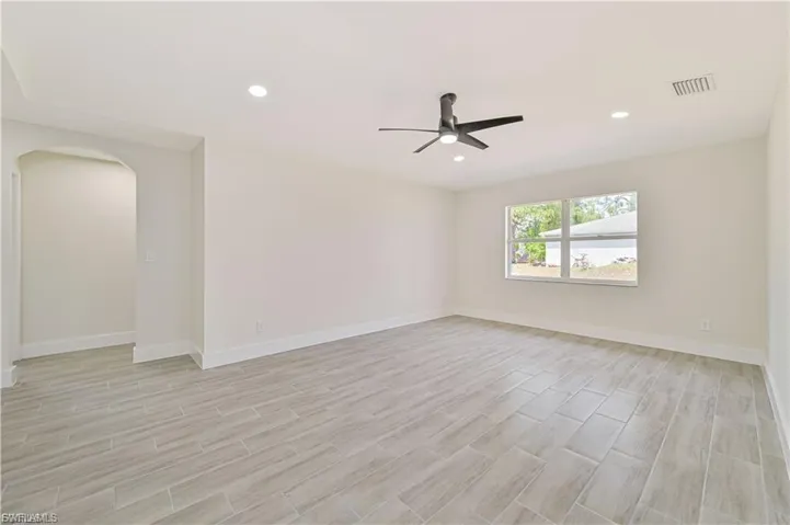 Empty room with arched walkways, wood tiled floors, ceiling fan, and recessed lighting