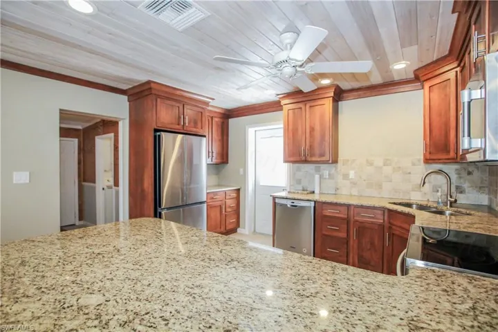 Kitchen with light stone counters, stainless steel appliances, backsplash, ceiling fan, and wooden ceiling