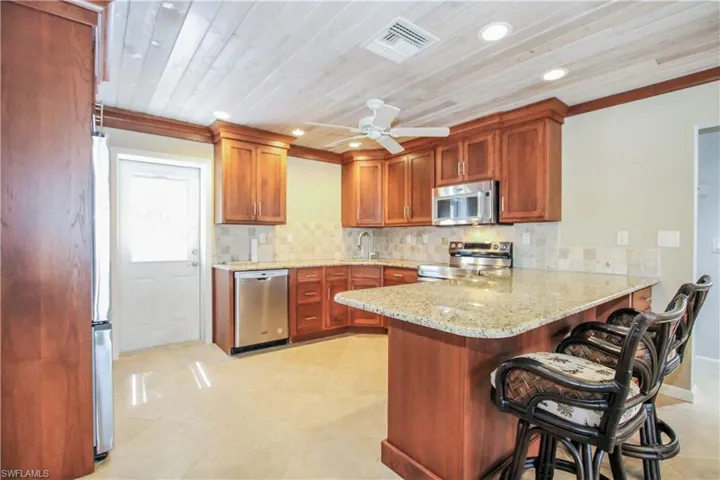 Kitchen featuring light tile flooring, stainless steel appliances, ceiling fan, wooden ceiling, and a breakfast bar