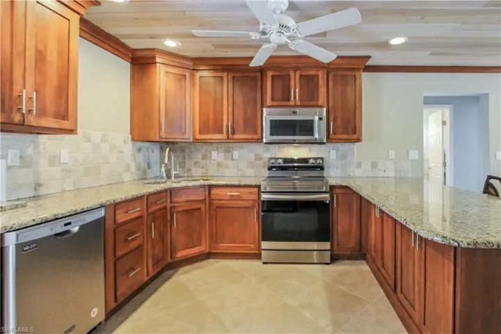 Kitchen with appliances with stainless steel finishes, wooden ceiling, kitchen peninsula, sink, and light tile floors