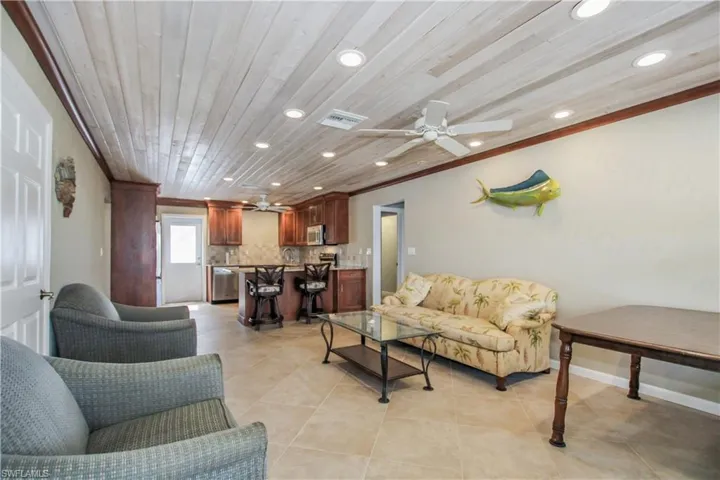 Tiled living room featuring ceiling fan, crown molding, and wood ceiling