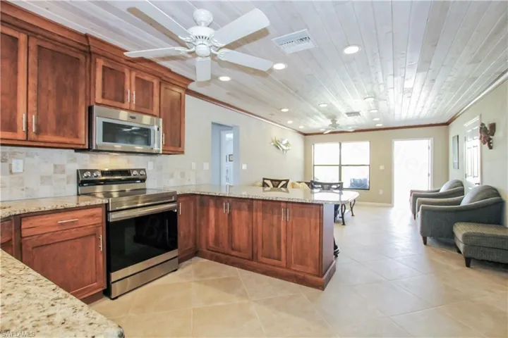 Kitchen with crown molding, light stone countertops, kitchen peninsula, and appliances with stainless steel finishes