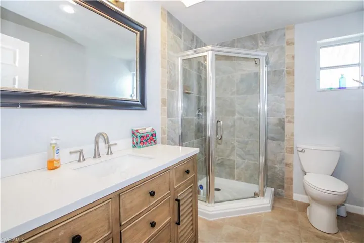 Bathroom featuring walk in shower, large vanity, toilet, and tile floors
