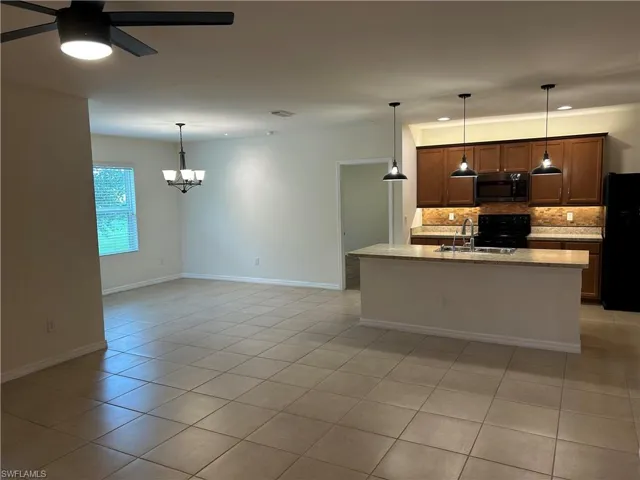 Kitchen with backsplash, black appliances, decorative light fixtures, a ceiling fan, and a kitchen island with sink