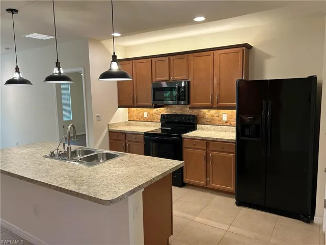 Kitchen with black appliances, light tile patterned floors, tasteful backsplash, decorative light fixtures, and light countertops