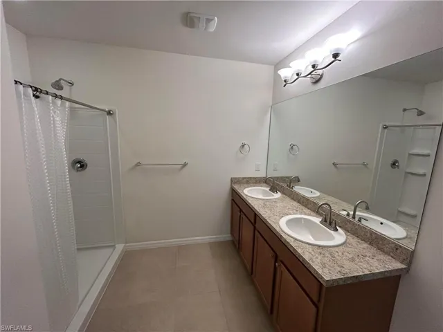 Bathroom with a stall shower, double vanity, and light tile patterned floors