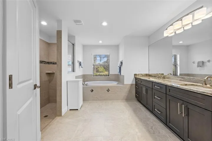 This primary bathroom features a large granite countertop with dual sinks, a walk-in tile shower, a separate water closet, and a large soaking tub.