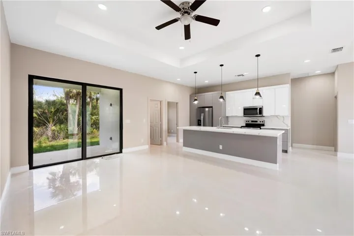 Kitchen with a tray ceiling, an island with sink, white cabinets, stainless steel appliances, and a ceiling fan