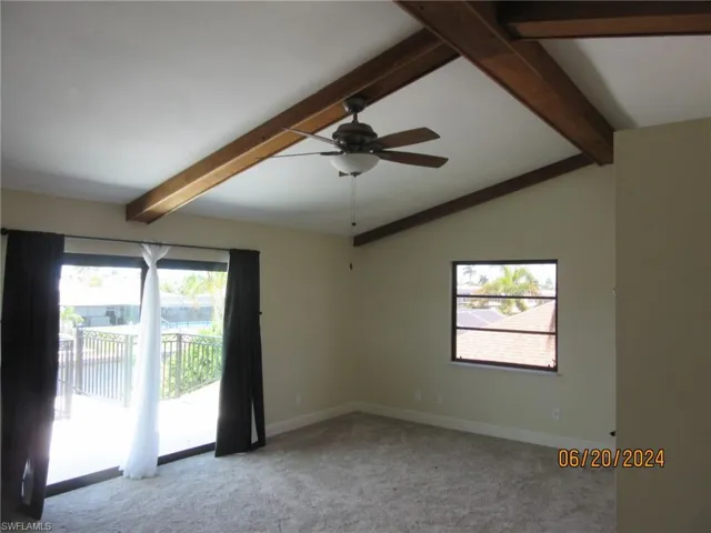 Carpeted empty room with lofted ceiling with beams and ceiling fan