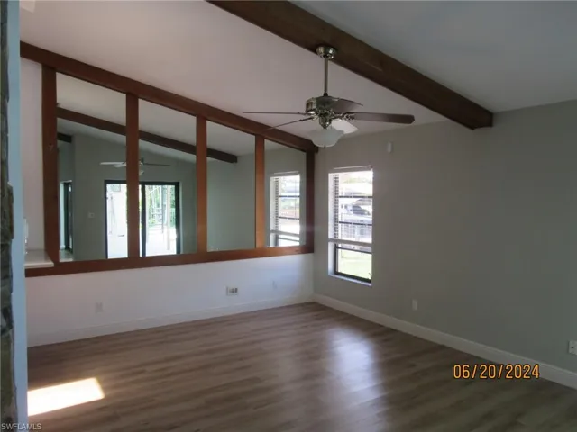 Empty room with wood-type flooring, a healthy amount of sunlight, and vaulted ceiling with beams