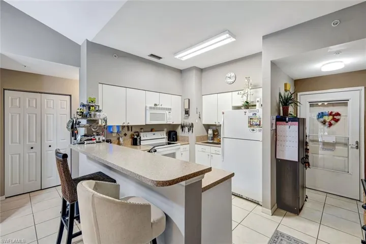 Kitchen featuring white appliances, light tile patterned floors, a kitchen bar, and a peninsula