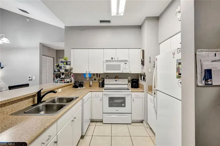 Kitchen with white appliances, white cabinetry, light countertops, and a peninsula
