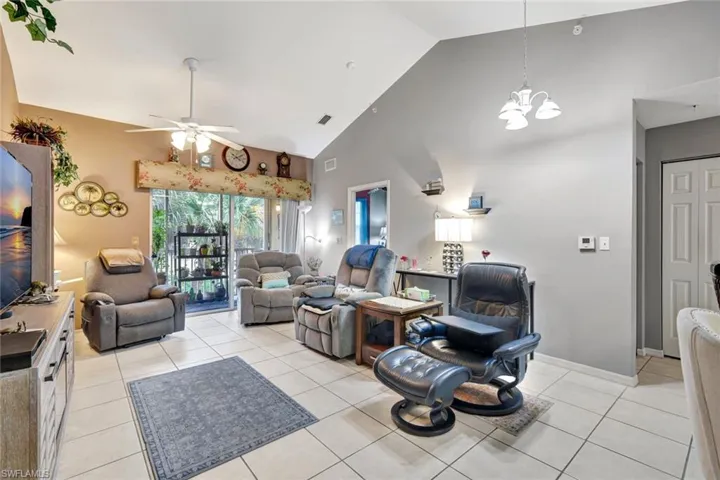 Living area with light tile patterned floors, high vaulted ceiling, ceiling fan, and a chandelier